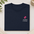 A folded navy blue t-shirt with a small pink puzzle piece graphic and the text 'something is missing.