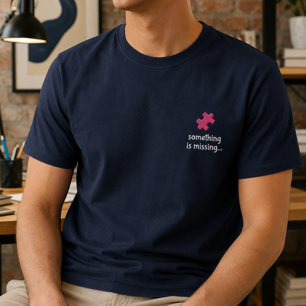 A man wearing a navy blue crewneck t-shirt with a pink puzzle piece graphic and the white text 'something is missing.