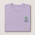 A folded light purple crewneck t-shirt on a light beige background, featuring a small green compass graphic and the text 'use your instincts' printed on the left chest.
